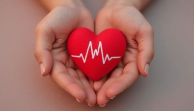 Hände halten ein rotes Herz mit einer weißen EKG-Linie, symbolisch für Gesundheit und Herzpflege.